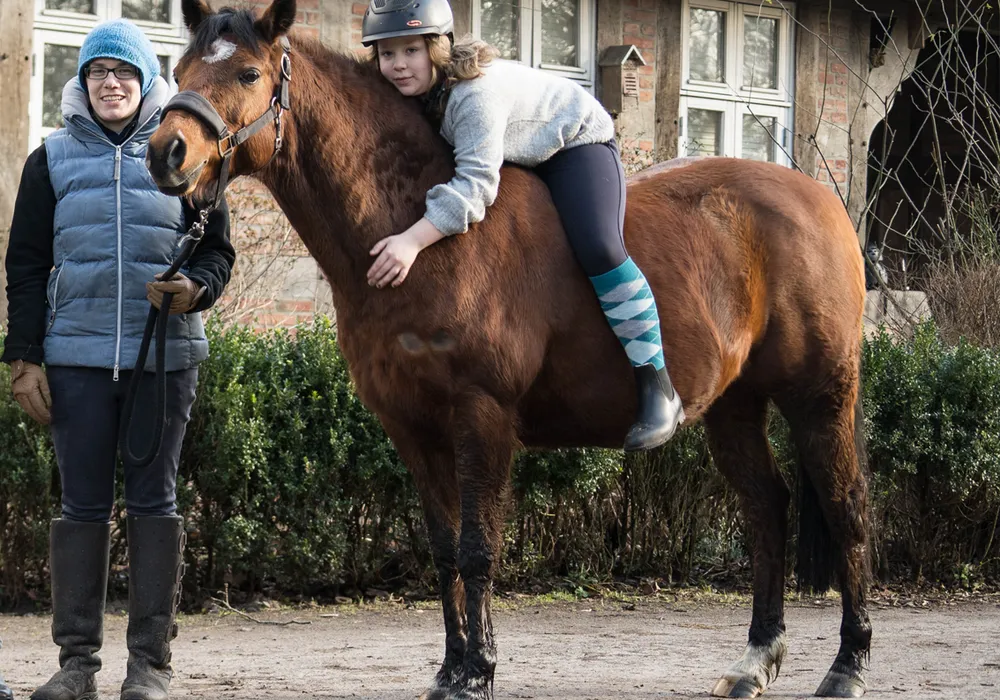 Reittherapie: Ein Kind liegt entspannt auf dem Rücken eines ruhig stehenden Pferdes