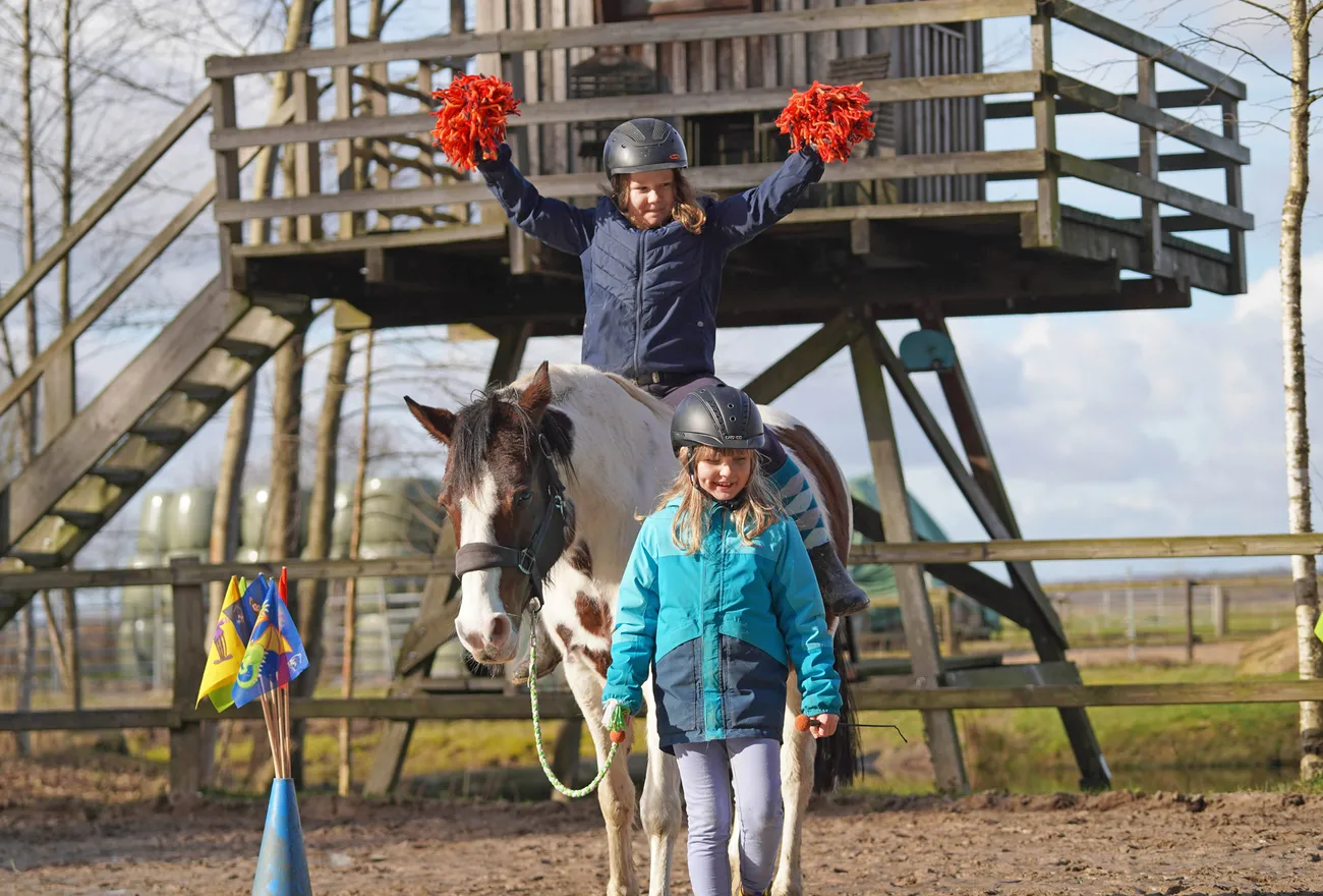 Ferienkurs auf dem Fabelhof: Kinder jubeln mit Pompons auf dem Kletterturm, ein Pony steht davor