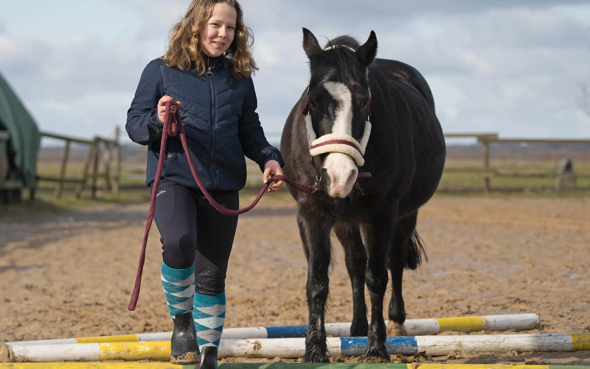 Ein Mädchen führt ein Pony über Bodenstangen auf dem Reitplatz des Fabelhofs