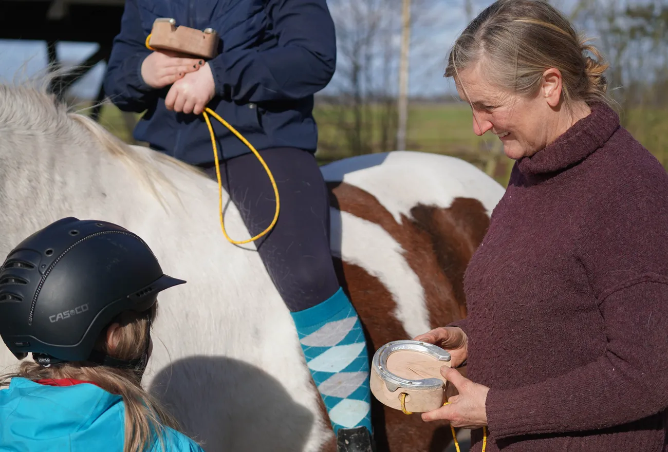 Hippolini-Unterricht: Die Trainerin belohnt das Schulpony, während zwei Kinder zuschauen