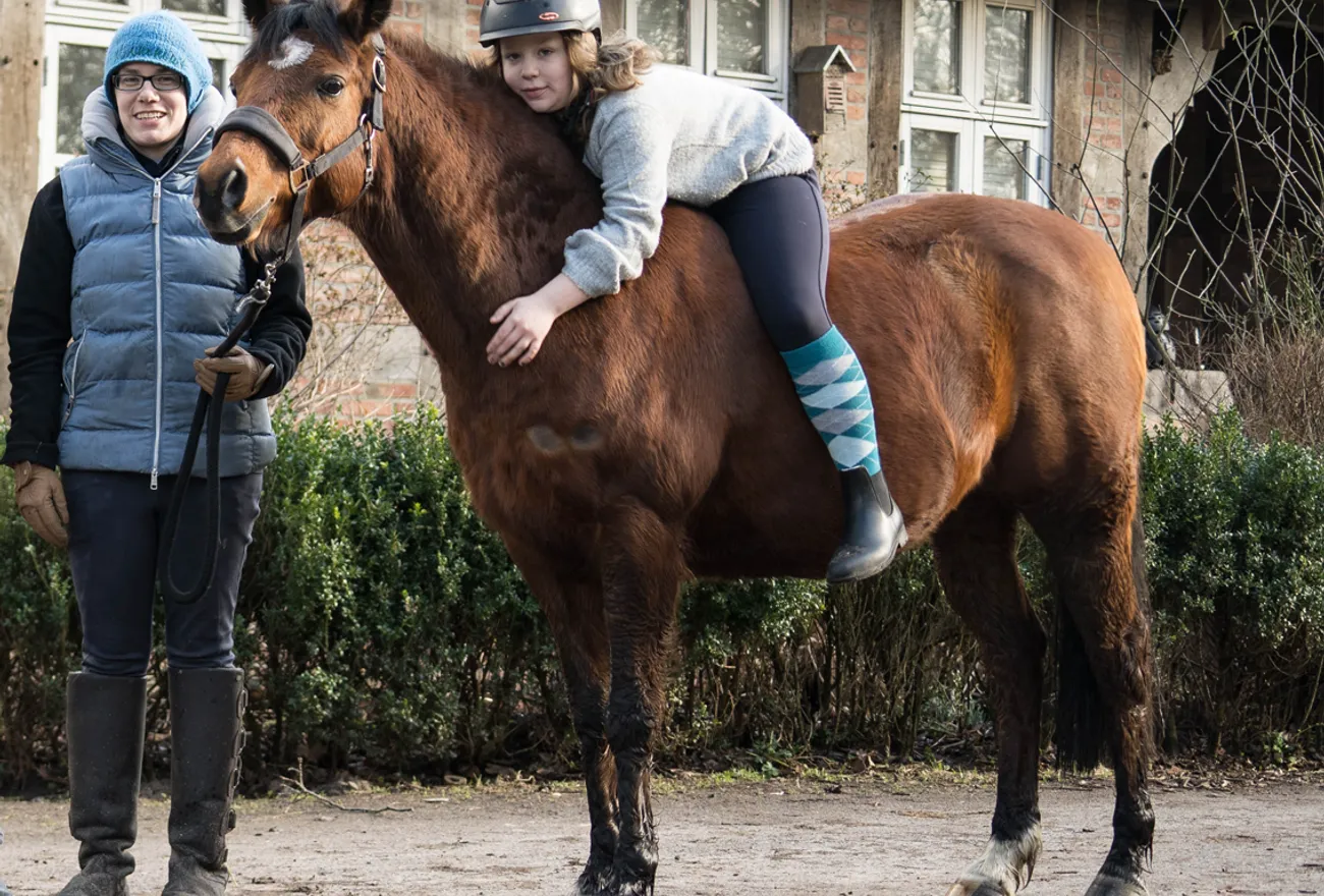 Reittherapie auf dem Fabelhof: Ein Kind liegt entspannt rücklings auf einem ruhig stehenden Pferd, begleitet von der Therapeutin